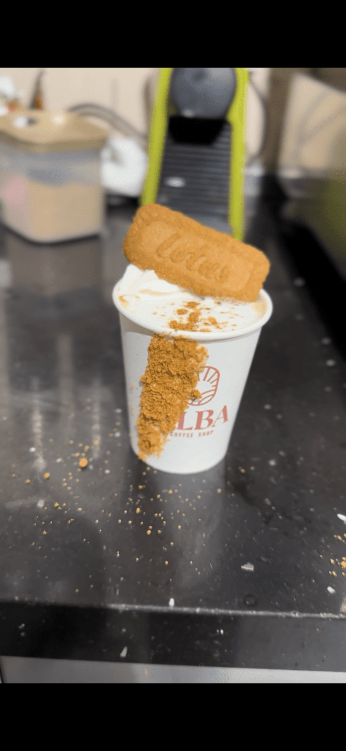 White coffee cup topped with whipped cream, a Biscoff cookie, and spilled cookie crumbs.