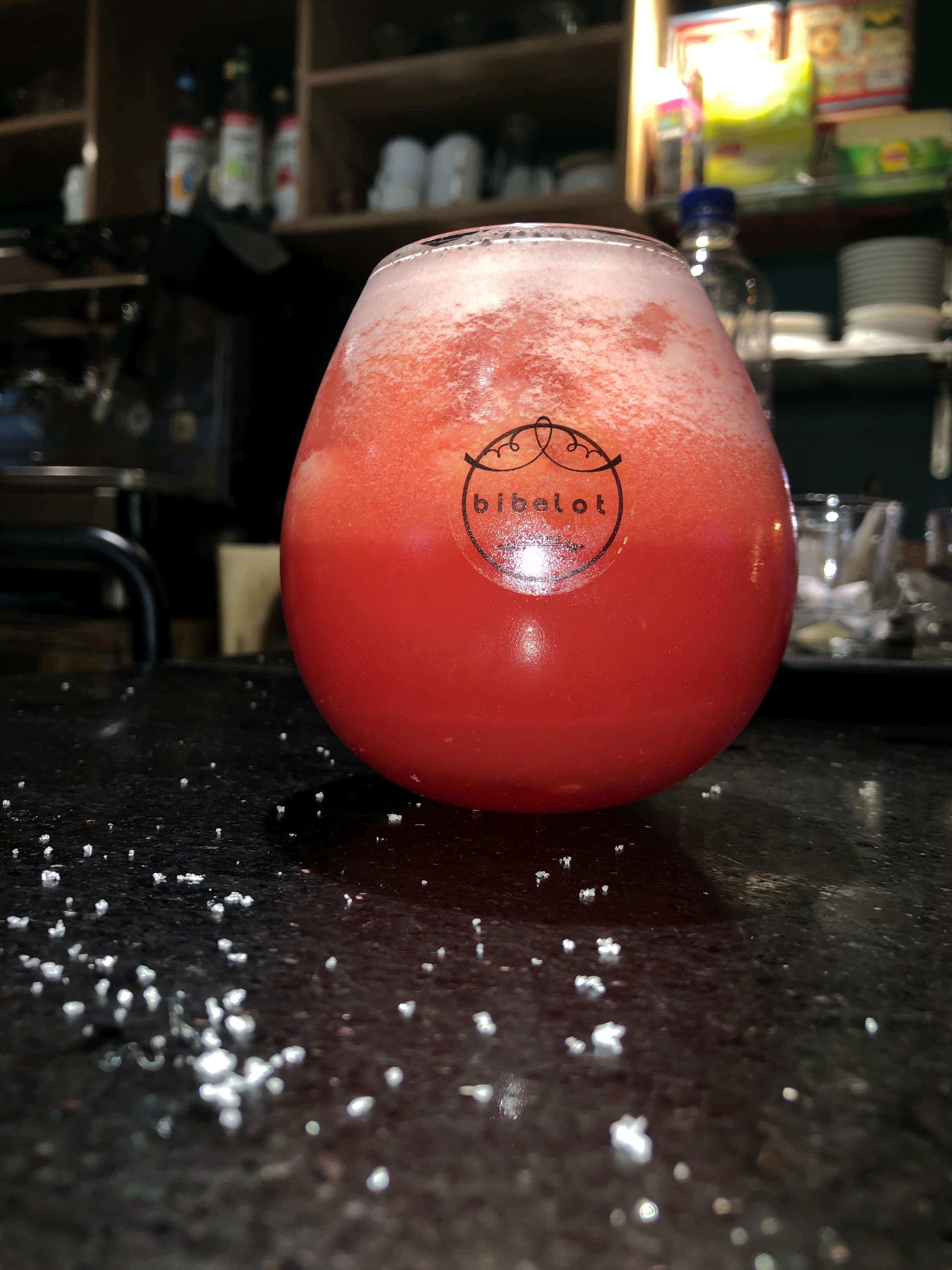 Frothy pink drink in a round bibelot glass on a dark, speckled bar counter.
